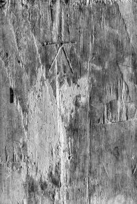 Black and white photograph of a weathered timber surface with peeling white paint and carved markings, exploring texture, materiality, and the quiet traces of time.